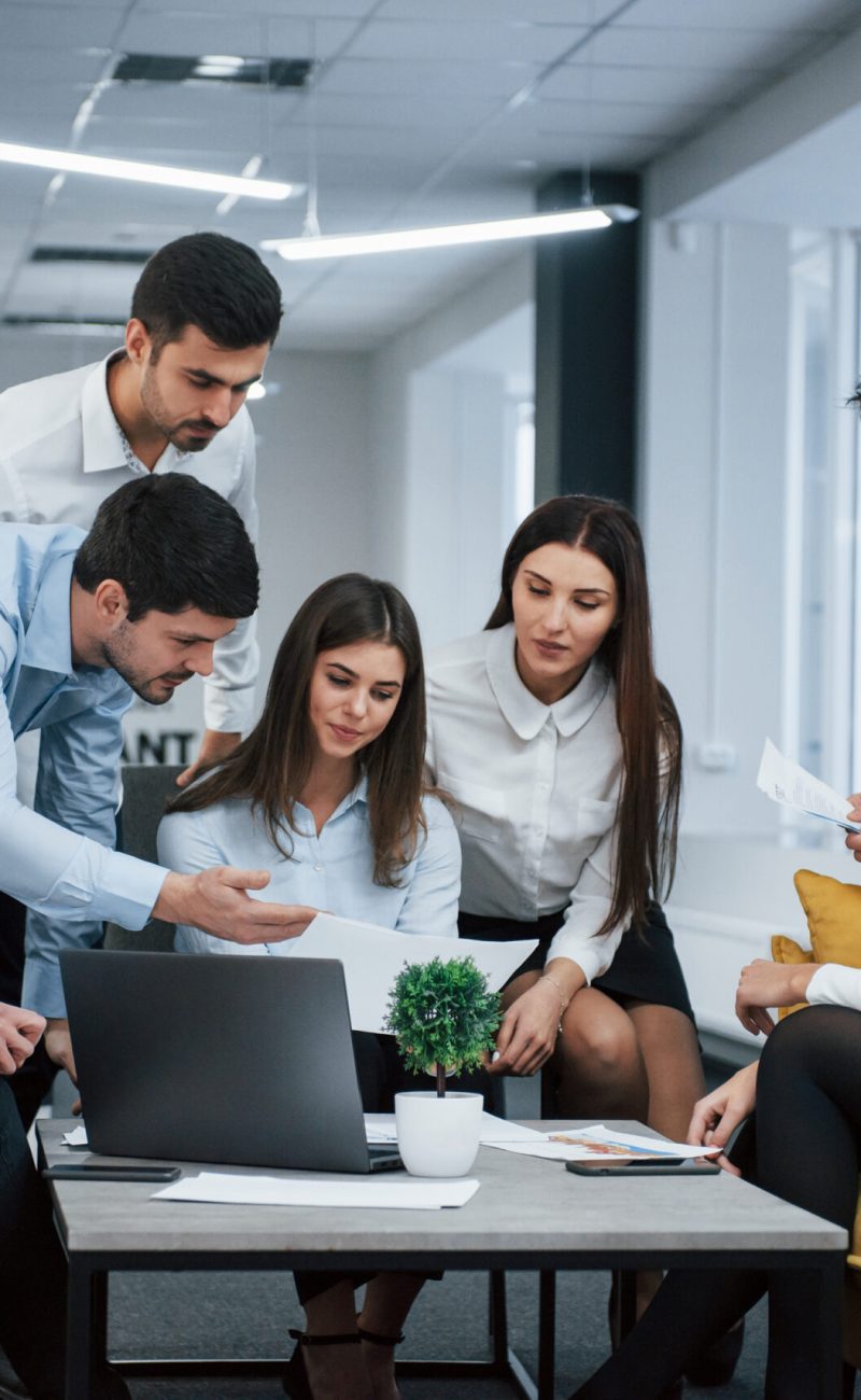 Guy shows document to a girl. Group of young freelancers in the office have conversation and working.
